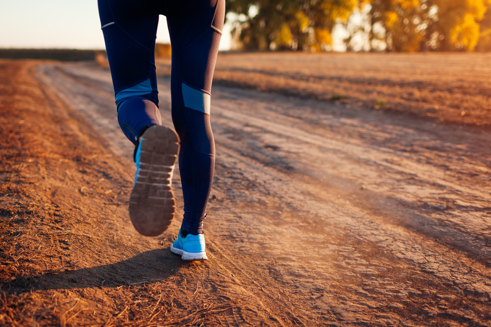 Woman running on a dirt road with her running shoes in focus.