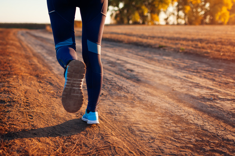 Woman running on a dirt road with her running shoes in focus.