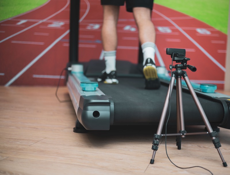 Runner performing a gait analysis on a treadmill with a tripod camera.