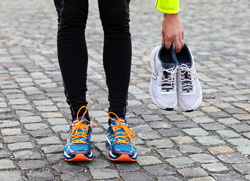 A runner holding used running shoes while wearing a new pair.