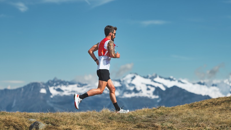 Man running on grass with a snowy mountain in the background.