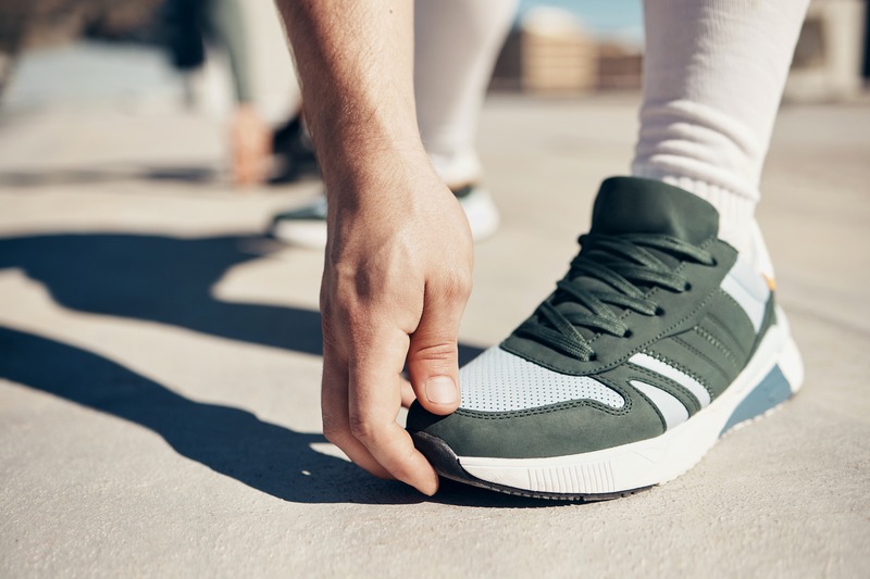 A runner bending down to touch the toe box of their running shoe.