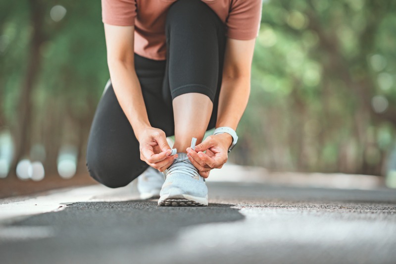 Woman runner kneeling on the pavement, tying her running shoes.