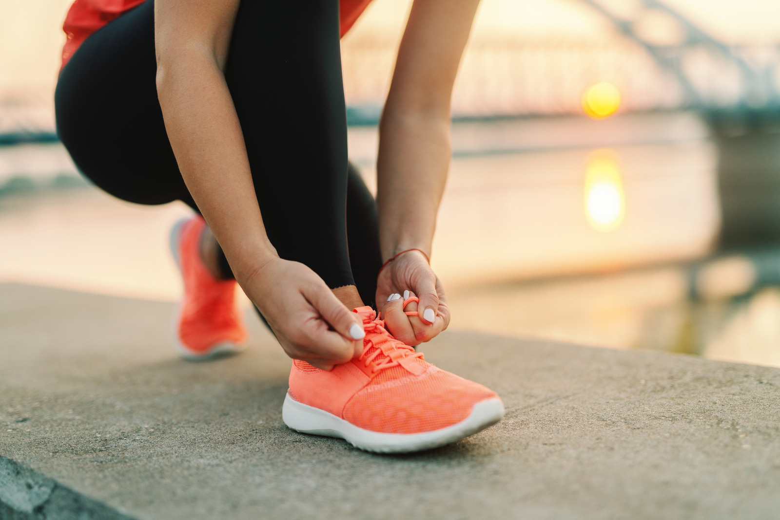 A woman crouching down and tying their running shoes.